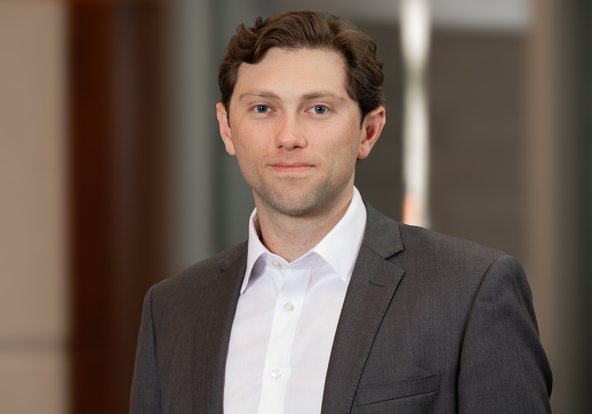 Professional headshot of a man in a gray suit and white shirt, with a neutral office background
