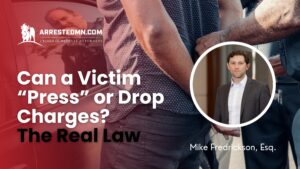 Banner for a legal article: 'Can a Victim Press or Drop Charges?' with a round-inset man in a suit on a red overlay background and the ArrestedMN.com logo.